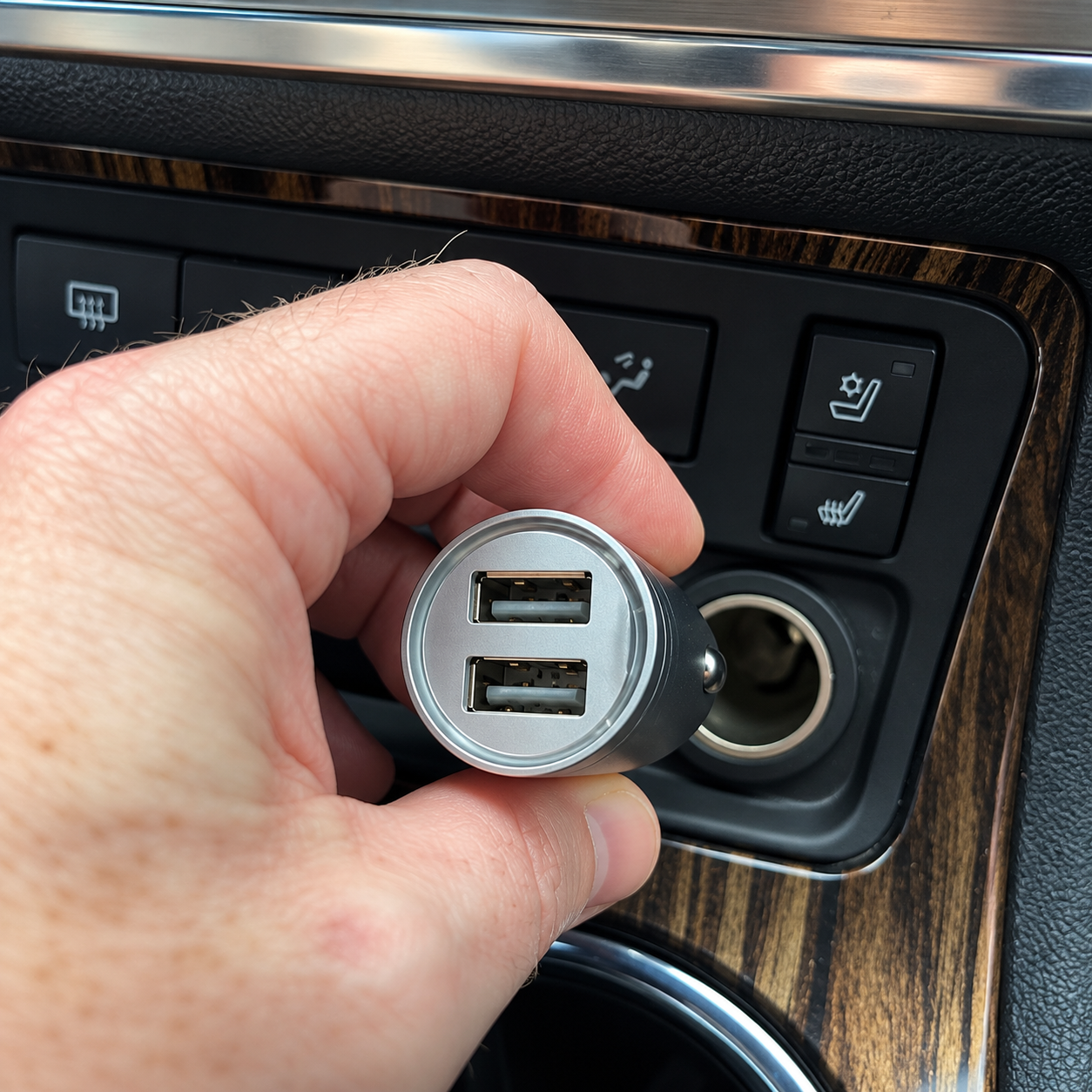 Dual USB car charger held near a vehicle 12V socket